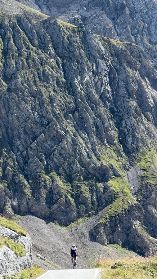 A lone rider tiny beneath a huge rock face on the Sanetsch