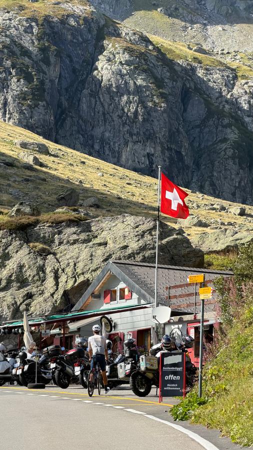 A rider stopping at the Sustenbrüggli café under a Swiss flag