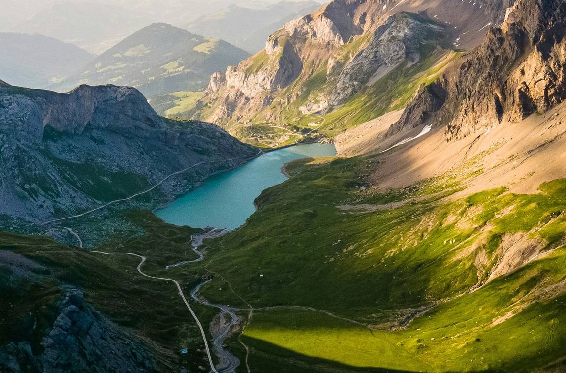 A road running past a turquoise alpine reservoir